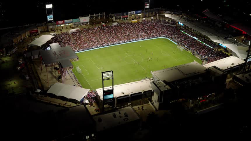 A nighttime aerial view of a soccer stadium with a game in progress and a large crowd watching from the stands