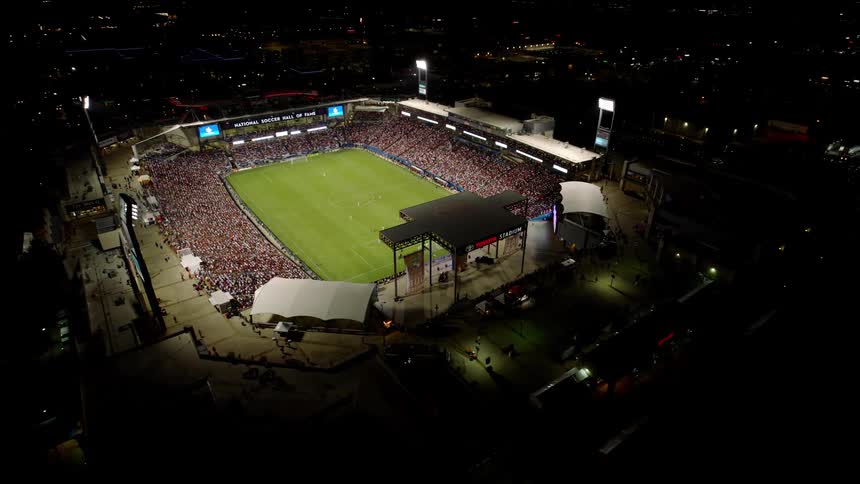 An aerial view of a packed soccer stadium during a match with a large crowd filling the stands