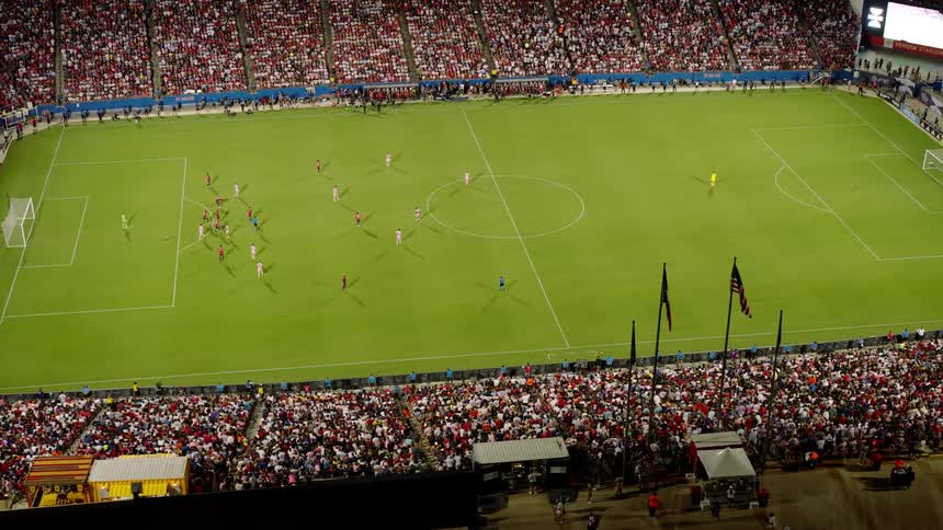An aerial view of a packed soccer stadium during a match with a large crowd filling the stands