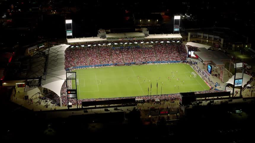 The soccer players run across the field as the fans watch