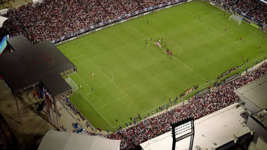 Soccer fans fill the seats of a stadium while the players stand on the field