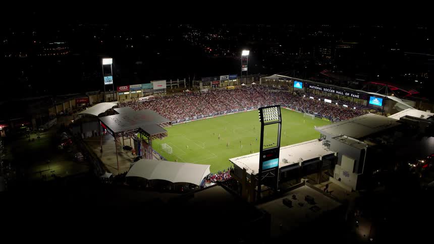 An aerial view of a packed soccer stadium during a match with a large crowd filling the stands