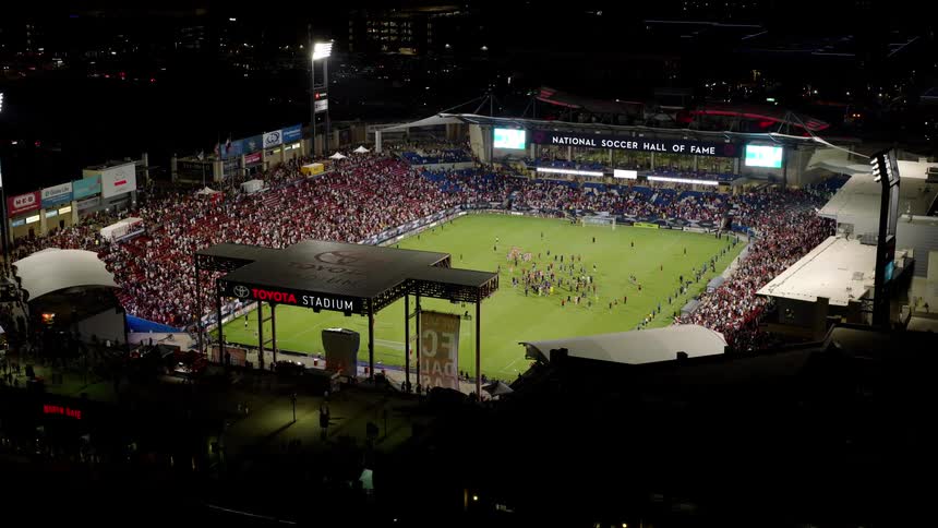 An aerial view of a large stadium with a green field and a grandstand full of people on a night