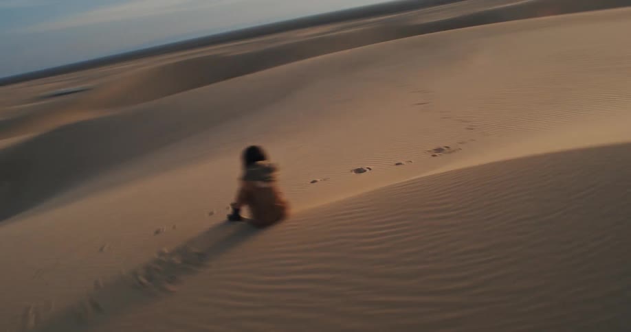 Woman sits on a dune in the desert on a cloudy day