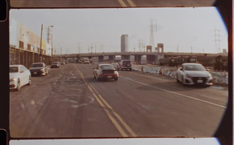 A vintage porsche driving on a city captured in vintage film from a drone