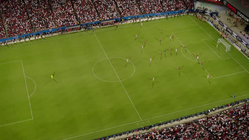 A soccer match in progress showing players on the field and a packed stadium of spectators