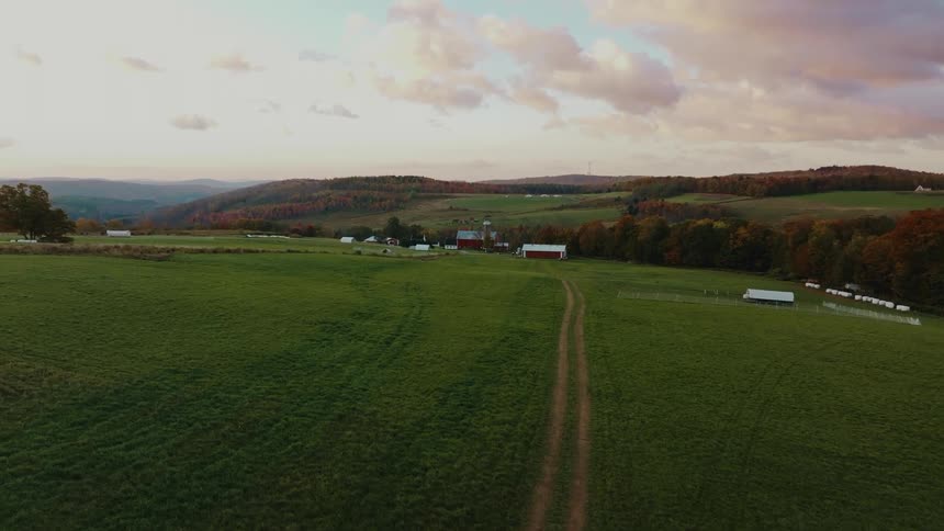 Aerial view of a farm nestled in a rolling valley with green fields a dirt road and a cluster of buildings in the distance