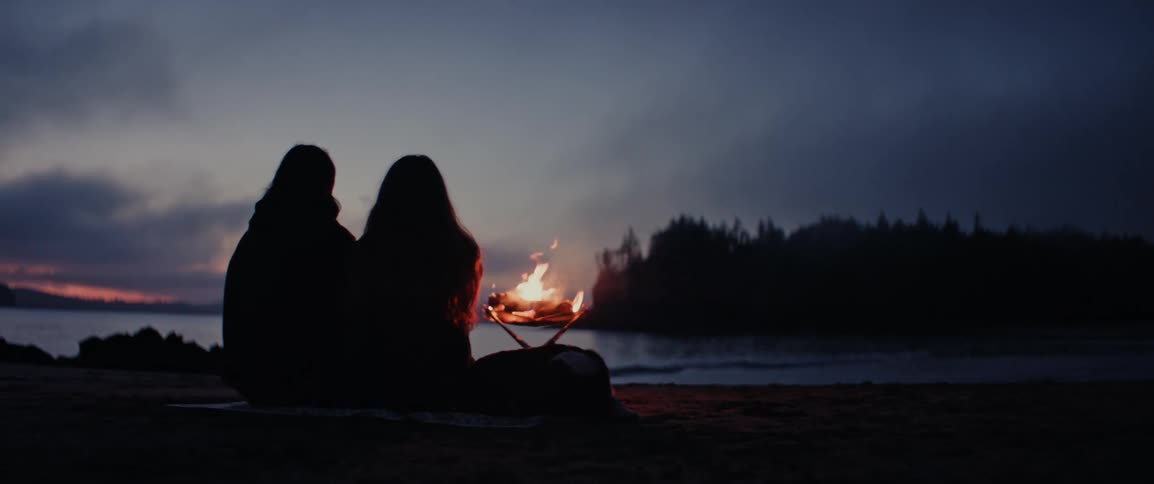 Silhouette of a couple sitting on the sand with a bonfire and the ocean in the background
