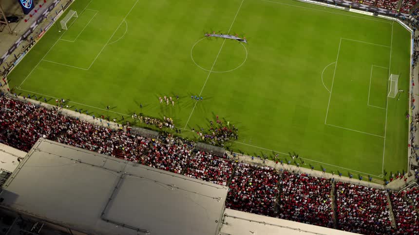 An aerial view of a packed soccer stadium during a match with a large crowd filling the stands