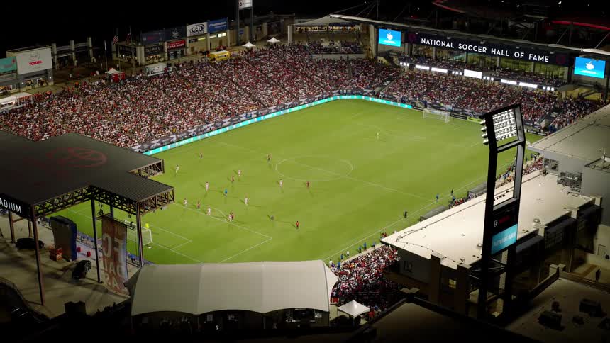 An aerial view captures a nighttime soccer match at a stadium showcasing a crowded crowd of spectators under the glow of stadium lights