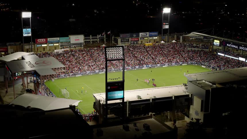 An aerial view of a packed soccer stadium during a match with a large crowd filling the stands