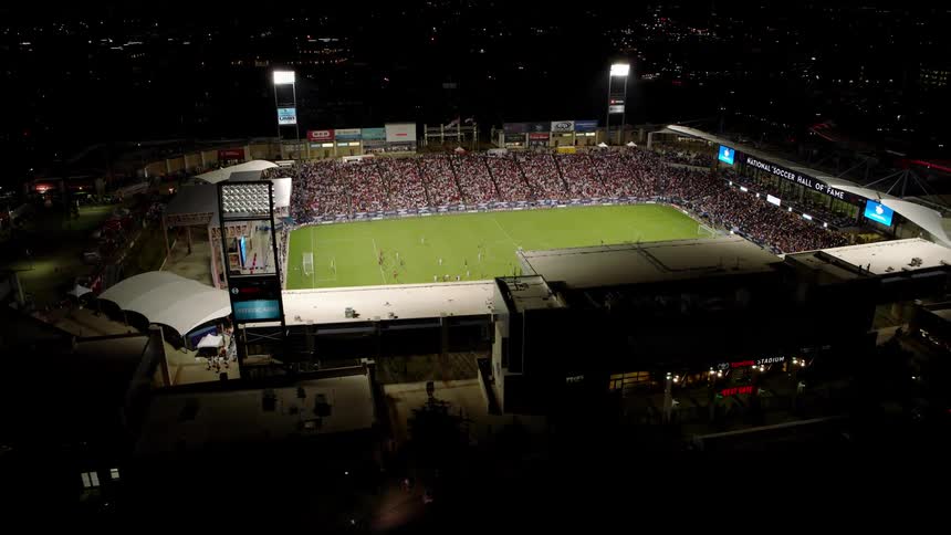 An aerial view of a packed soccer stadium during a match with a large crowd filling the stands