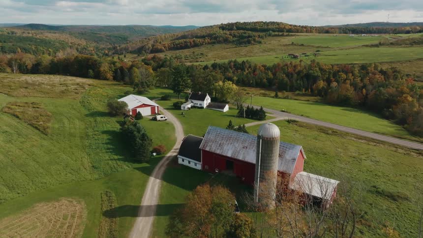 A sprawling farm nestled in a picturesque valley with rolling hills a dirt road leading to a red barn and silo and a farmhouse surrounded by lush green fields