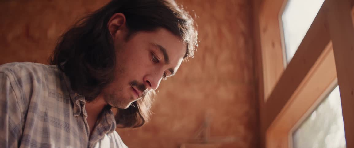 A man is looking down at his craft while standing near a window in a work shop