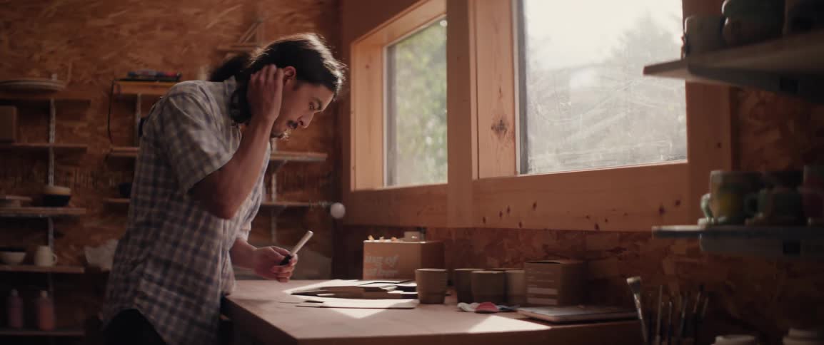 A person is working with pottery in a welllit workshop surrounded by shelves filled with various ceramic items and tools