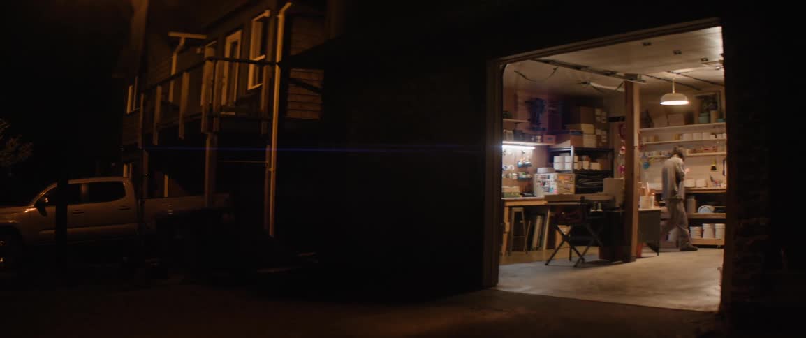 A person walking inside a workshop with the door open on a dark night