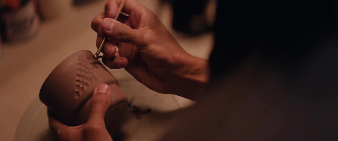 A person is carving a design into a clay cup