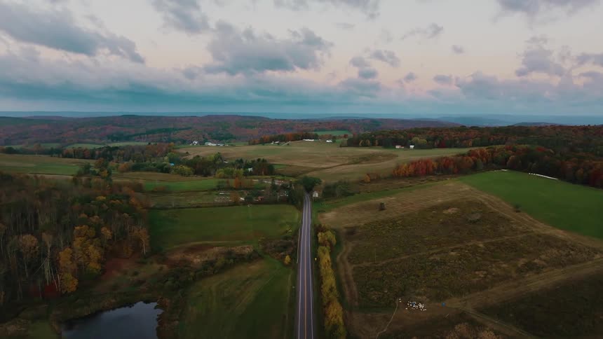 An aerial view of a scenic countryside with rolling hills farms and a road snaking through the landscape