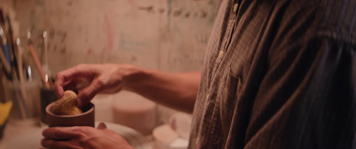 Male potter shapes a cup using a sponge in his workshop