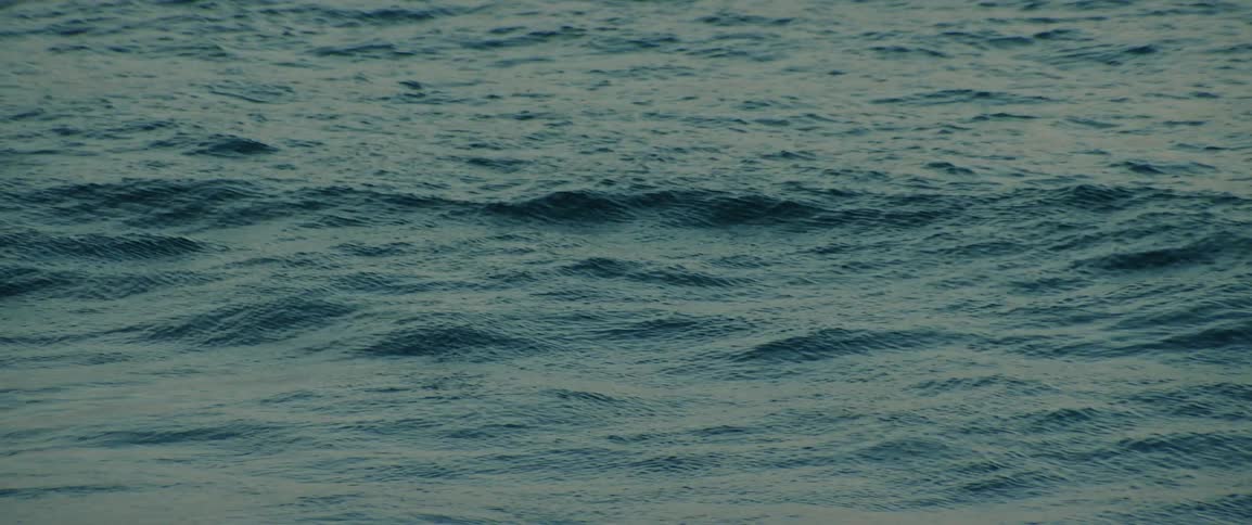 The ocean surface moves with gentle waves in twilight
