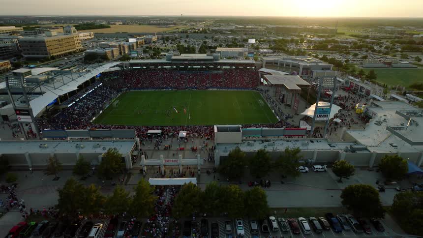 An aerial view of a large packed stadium during a sporting event at sunset