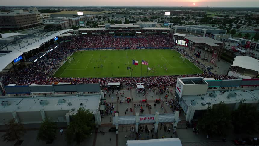 Fans fill a texas stadium for a soccer game at sunset