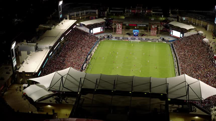 A large stadium with a green field and stands full of people on a night seen from above
