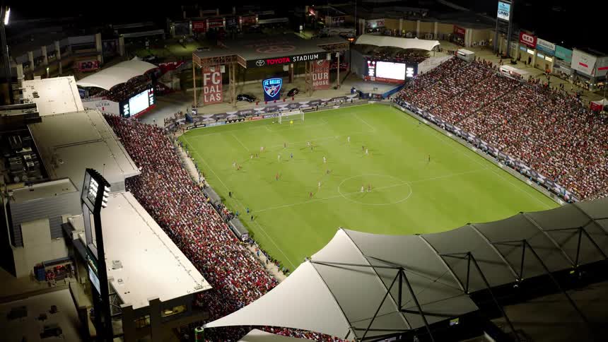 A night time shot of a soccer game in progress at a stadium illuminated by lights and packed with spectators
