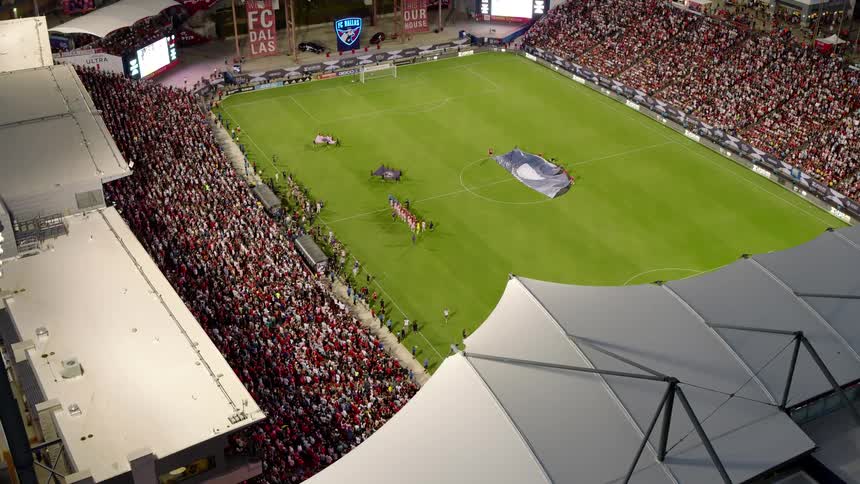 An aerial view of a packed soccer stadium during a match with a large crowd filling the stands