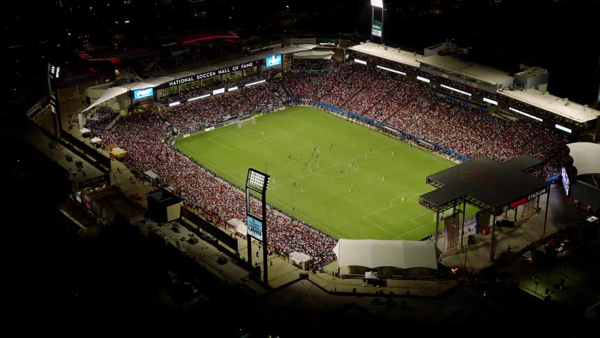 Sports fans crowd the stands at a soccer game at night in the city
