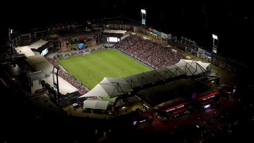 An aerial view of a large sports stadium with a green lawn and a grandstand full of people at night
