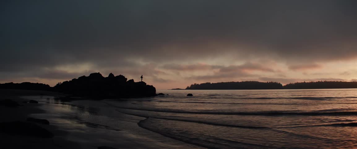 Calm sea waves wash up on the shore under a dark cloudy sky at dusk