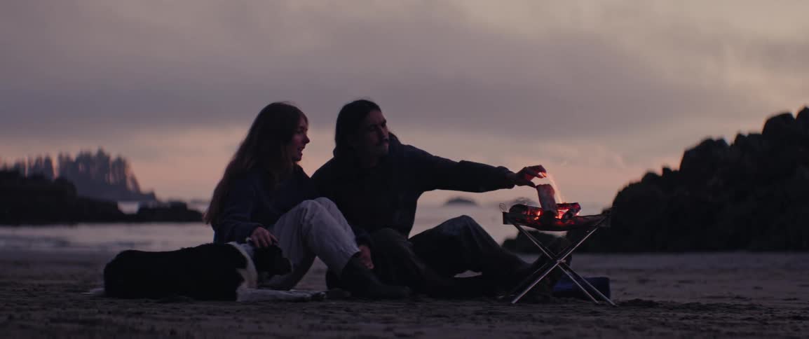 A clip a couple sitting beside a camp fire on the beach