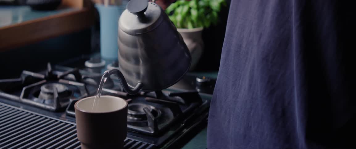 Hand picking up a kettle and pouring hot water into a mug