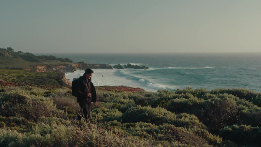 Man with a backpack walking along the coast with the sea in the background