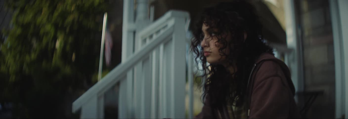 Young woman sitting on the porch steps while braiding a bracelet moves over to let a male friend sit