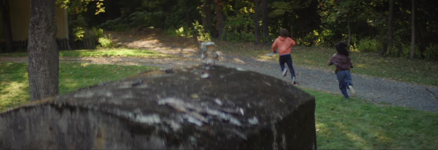 A couple of kids hide behind a wall filming with a handheld camera before running away