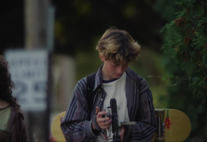 Teenagers walk together while the boy looks at his camera