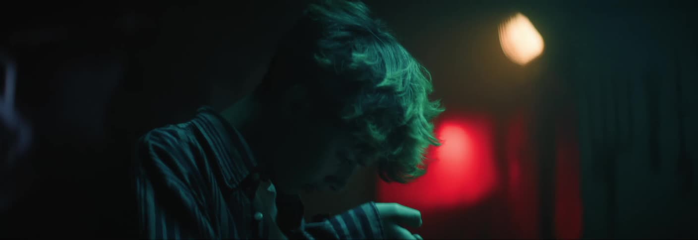 A person is handling a video camera in a dimly lit area before looking up the camera panning to the window revealing a woman motioning to the other person
