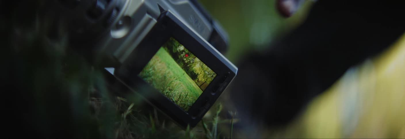 A person walking up to a camera that has the camera pointed at the grassy ground and the person picks it up