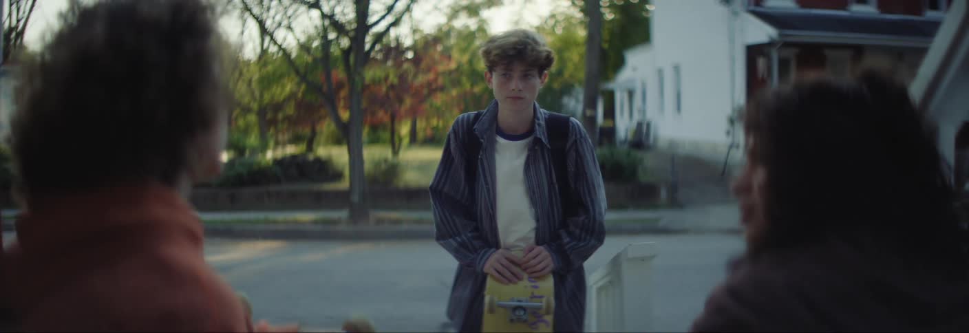 A group of teenagers with skateboards talking on a calm neigborhood street at morning