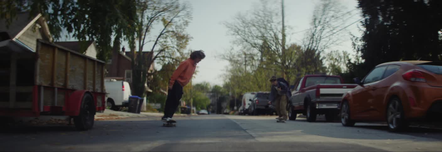 Two teenagers skateboard down the street past the homes
