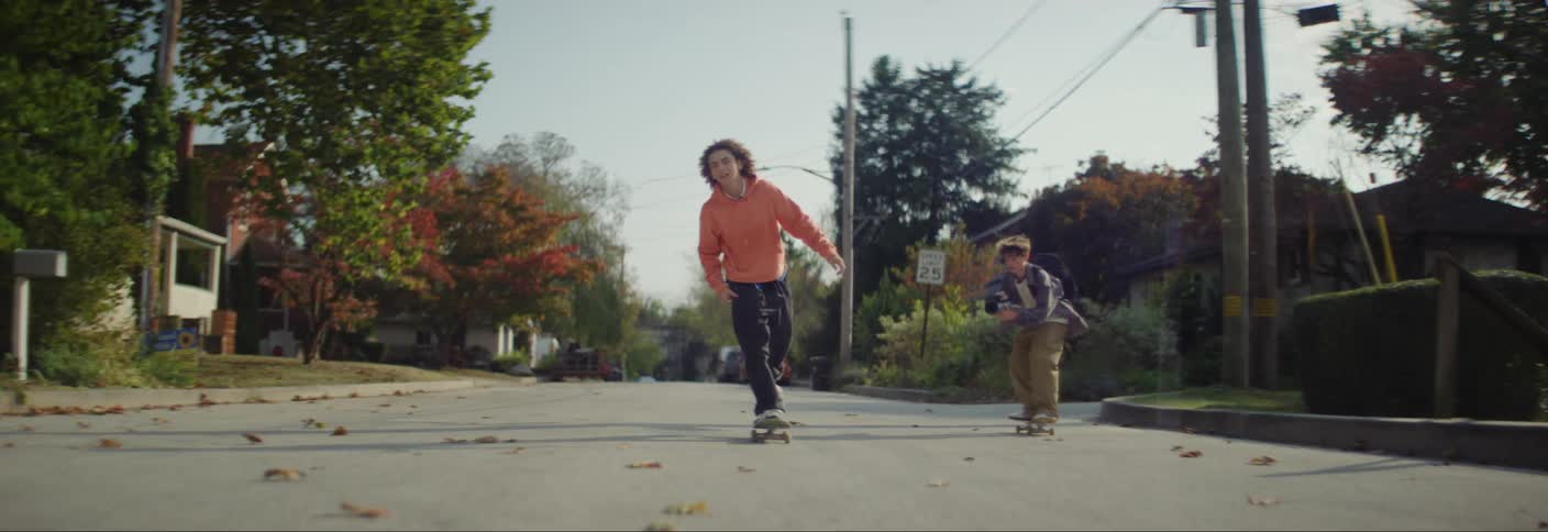Do teenage boys skateboard down a residential tree lined street