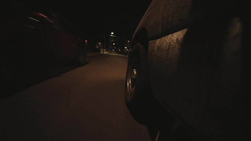 A nighttime street scene captured from a low angle showing the side of a moving vehicle with streetlights illuminating the road ahead
