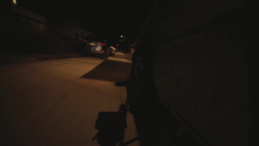 Car drives along a street with several parked vehicles at night