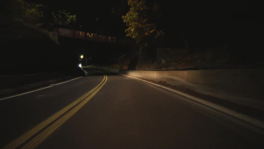 A car travels down a winding road at night illuminated by its headlights