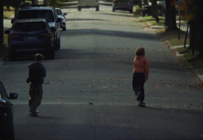 Two children are on a street riding skateboards