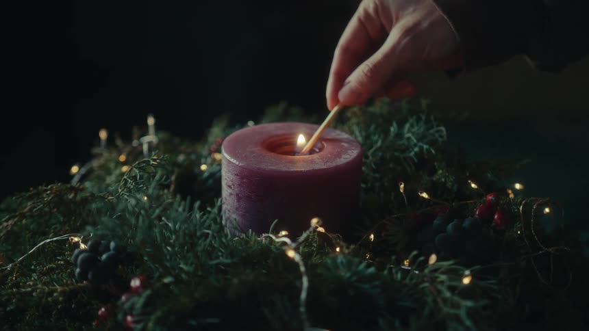 A man lights a candle sitting on the wreath