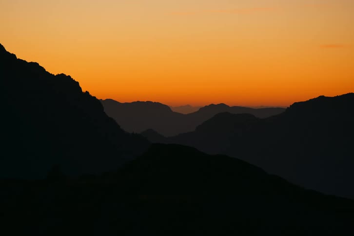 Silhouetted against a fiery orange sunset a mountain range stretches across the horizon