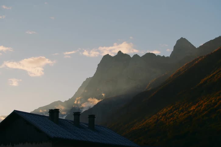 A small house with a roof with some chimneys and backs onto a large mountainous region